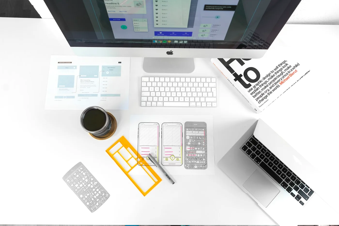 A design workspace with interface layouts on a monitor and wireframe sketches on the desk