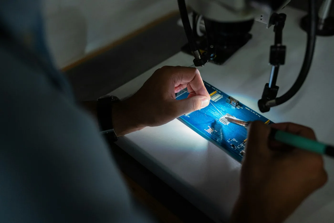 Hands repairing a small electronic circuit beneath a microscope
