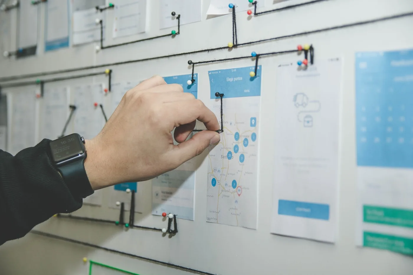 A hand arranging interface sketches and notes on a planning wall